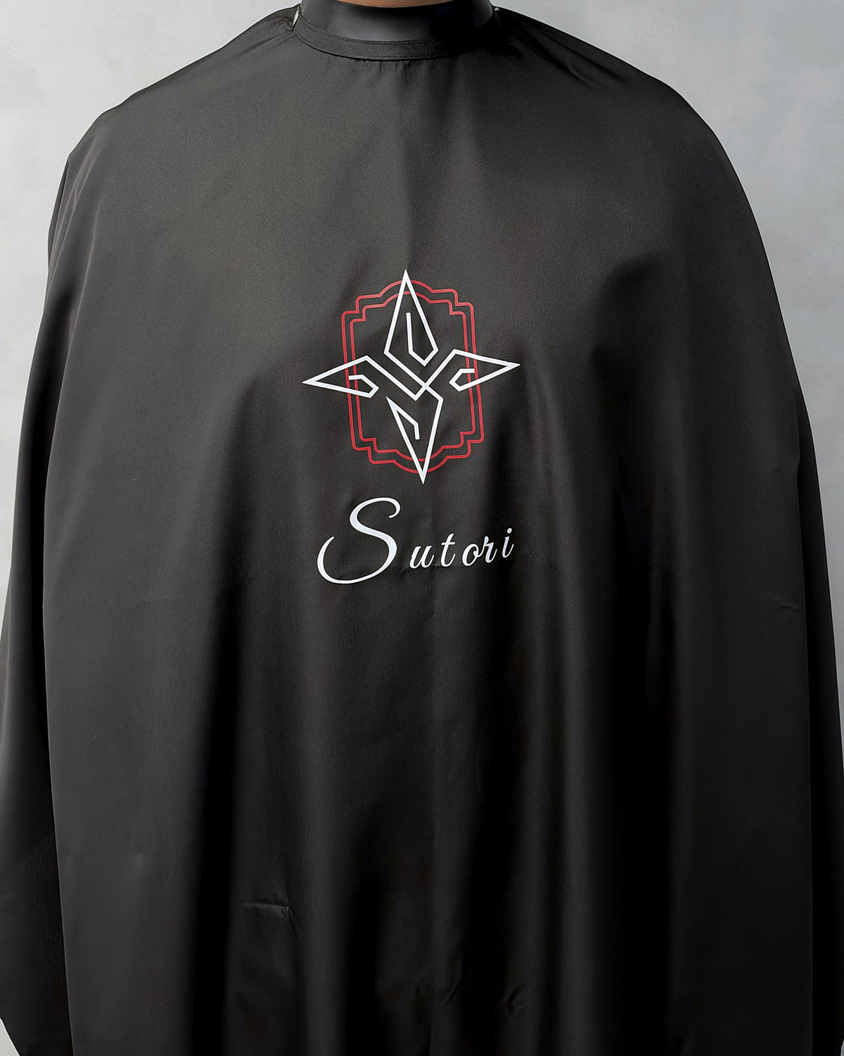 Black Sutori barber cape worn, from the front, with the Sutori crest and name